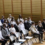 Uczniowie siedzący na krzesłach na sali gimnastycznej